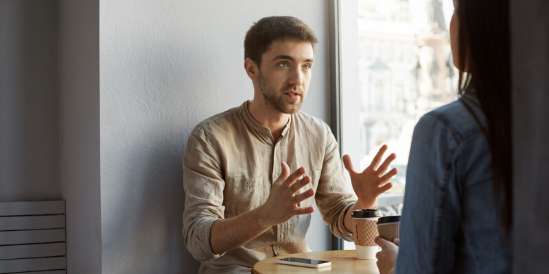 serious unshaved dark haired man sitting cafeteria with client talking gesticulating with hands trying make clear some details commission he received v4